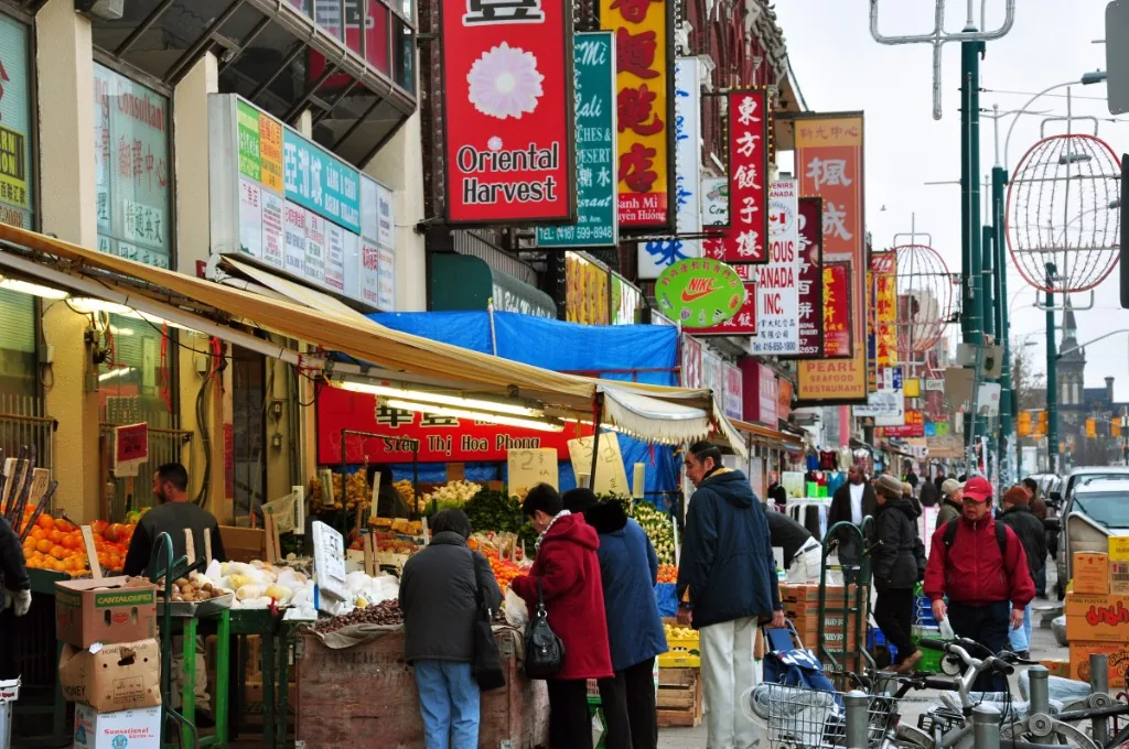 Stacked signage above busy market stalls on Spadina Avenue