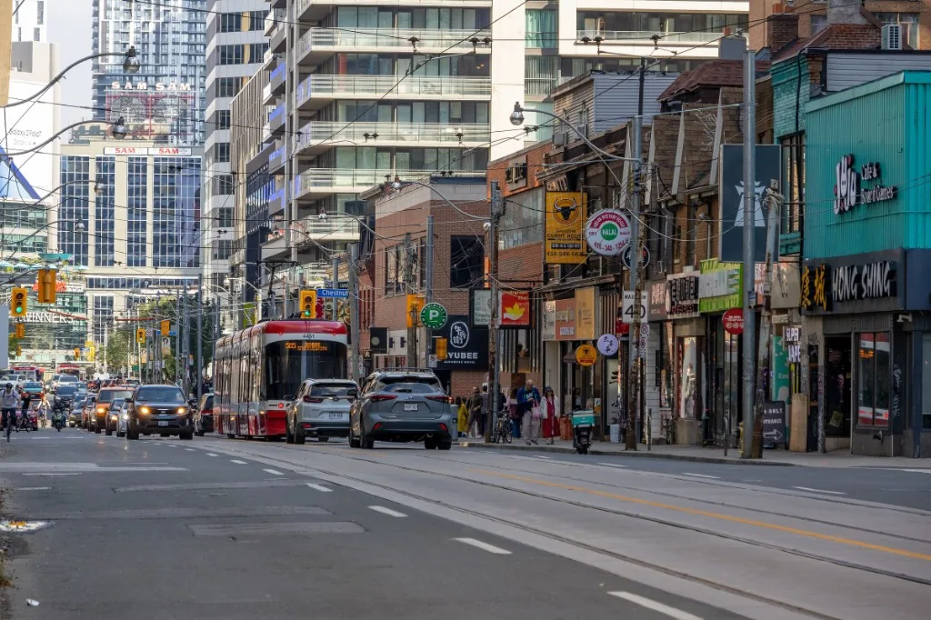 A red streetcar moving down Dundas Street West past low storefronts