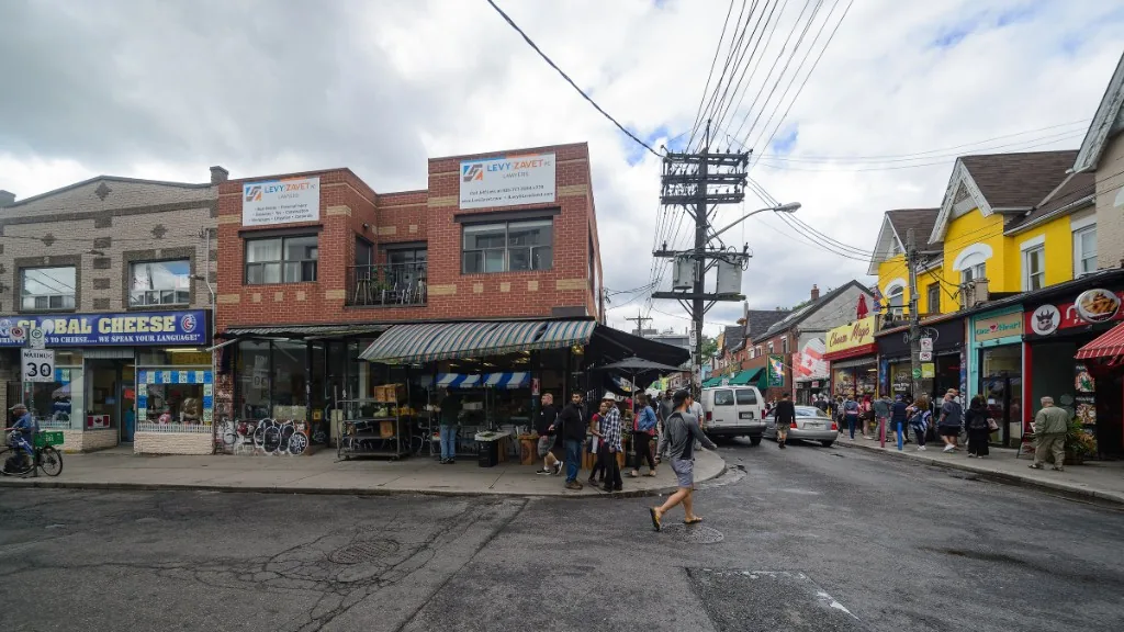 A busy Kensington Market corner with shops and people crossing the street