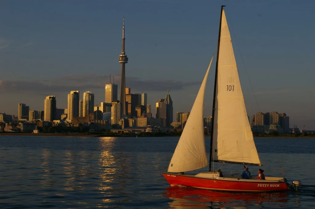 A small red sailboat crossing the harbour with the skyline behind it